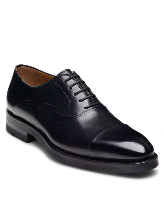 The Magnanni Omega in Black is a single leather Oxford shoe, crafted from premium calfskin featuring a timeless design with a closed lacing system and polished cap toe, elegantly set against a white background.