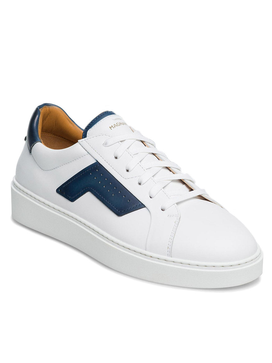 Introducing the Magnanni Phoenix in White/Navy: a white low-top with blue accents on the heel and side, featuring a thick white sole and white laces. With its leather accents, this shoe effortlessly combines style and sporty appeal.