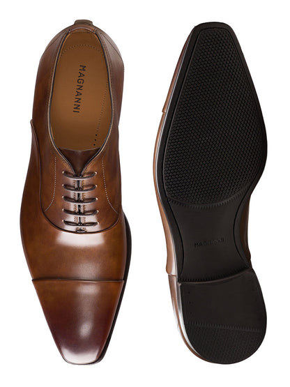 The Magnanni Santiago in Tabaco men’s leather oxford dress shoes are shown from the top and bottom, featuring a closed lacing system, cap toe design, and rubber sole detail.