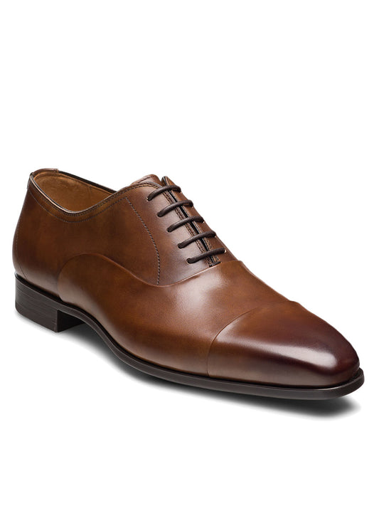 The Magnanni Santiago in Tabaco is a luxury brown leather men’s oxford with a classic cap toe, closed lacing, and low heel—ideal for elevating any formal outfit.