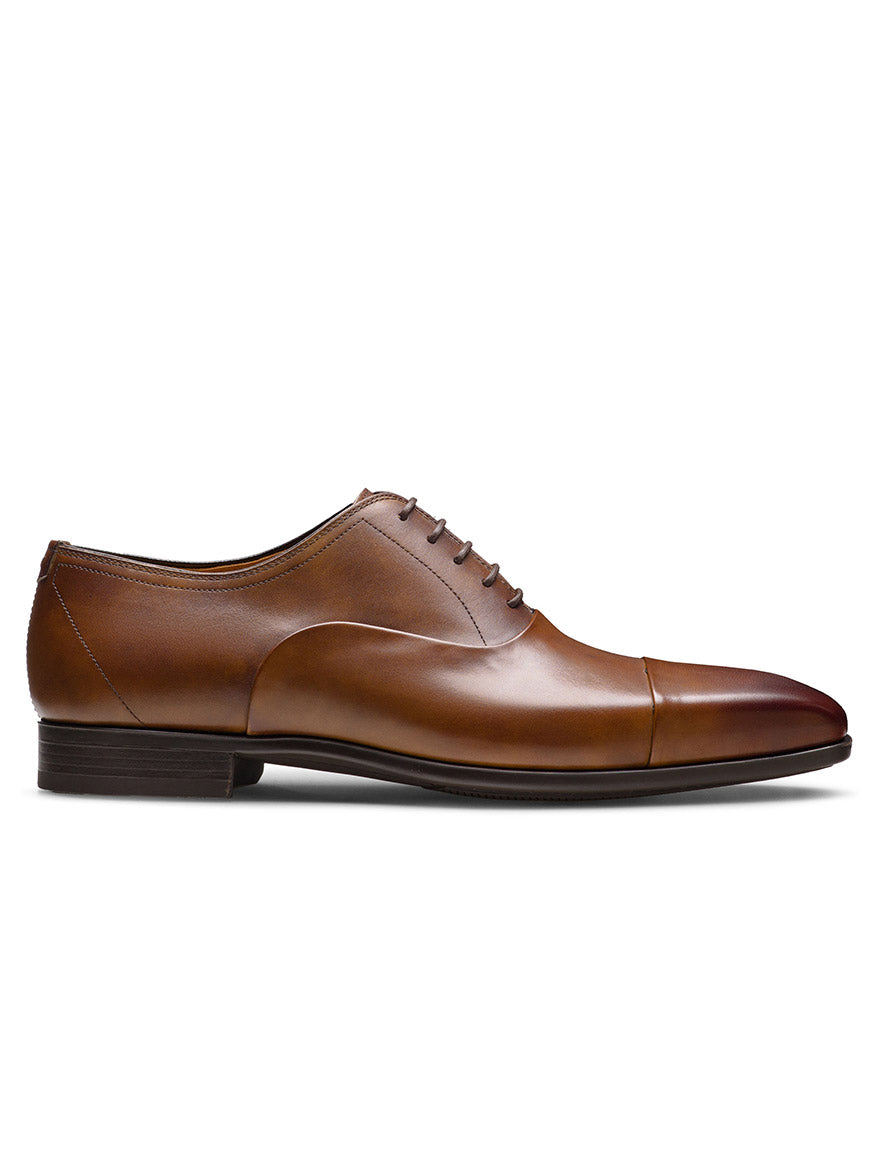 The Magnanni Santiago in Tabaco is a brown men’s leather oxford with a cap toe, closed lacing, and low heel, elegantly displayed in side profile on a white background—ideal for any formal occasion.