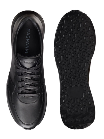 A pair of Magnanni Syros in Black sneakers, made in Spain with luxurious leather, shown from top and sole views, featuring a lace-up design and textured rubber outsole.