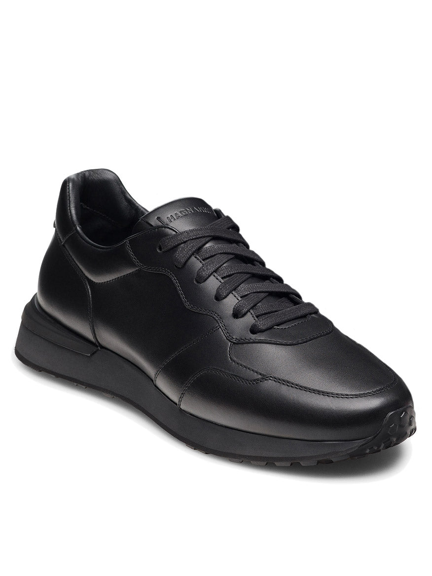The Magnanni Syros in Black is a luxurious leather sneaker crafted in Spain, featuring black laces and a low rubber sole, displayed at an angle on a white background.