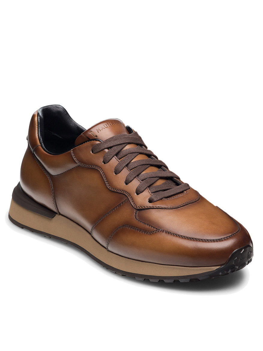 The Magnanni Syros in Brown is a luxurious leather sneaker made in Spain, featuring dark brown laces, a black and tan rubber sole, and refined stitching for an elevated style.