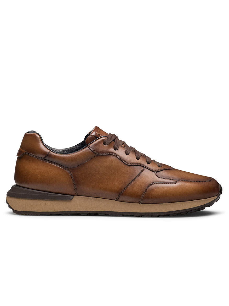 The Magnanni Syros in Brown is a low-profile running sneaker featuring brown leather, matching laces, and a rubber sole, displayed in a side view against a white background.
