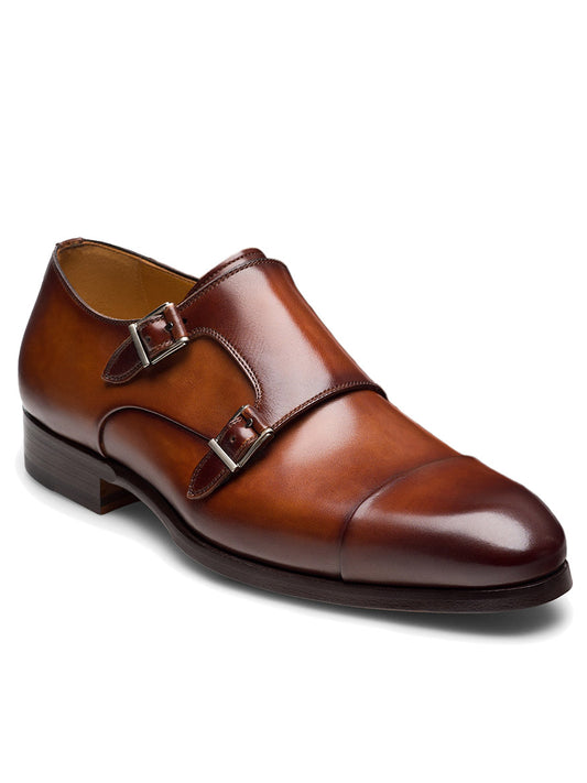 The Magnanni Tinos in Cognac is a brown leather double monk strap dress shoe with a sleek cap toe, two metal buckles, and a low heel, displayed on a white background.