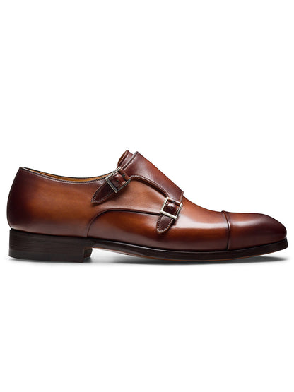 The Magnanni Tinos in Cognac is a brown leather double monk strap dress shoe with a cap toe, low heel, and polished finish, shown in profile on a white background.