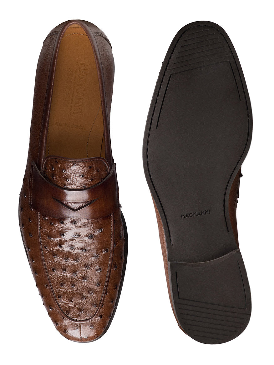 The Magnanni Viggo in Tabaco is a pair of handcrafted men's penny loafers in brown leather with textured uppers and smooth black soles, shown from top and bottom views.