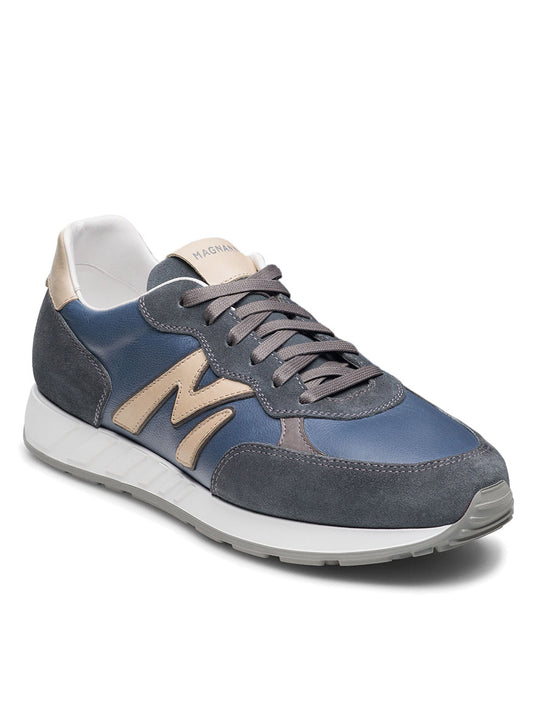 The Magnanni Yoki in Indigo Suede/Cream is a retro-inspired sneaker with a blue and gray design, gold "M" logo, white midsole, and gray laces. Its timeless aesthetic pairs with an athletic sole for comfort and style.