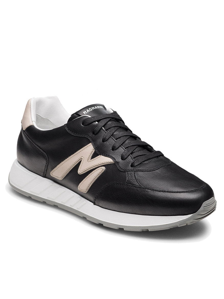 The Magnanni Yoki in Black/Cream is a retro-inspired sneaker with black leather, cream accents, a white athletic sole, and a bold cream "M" logo on the side—crafted in Spain and shown at an angled view.
