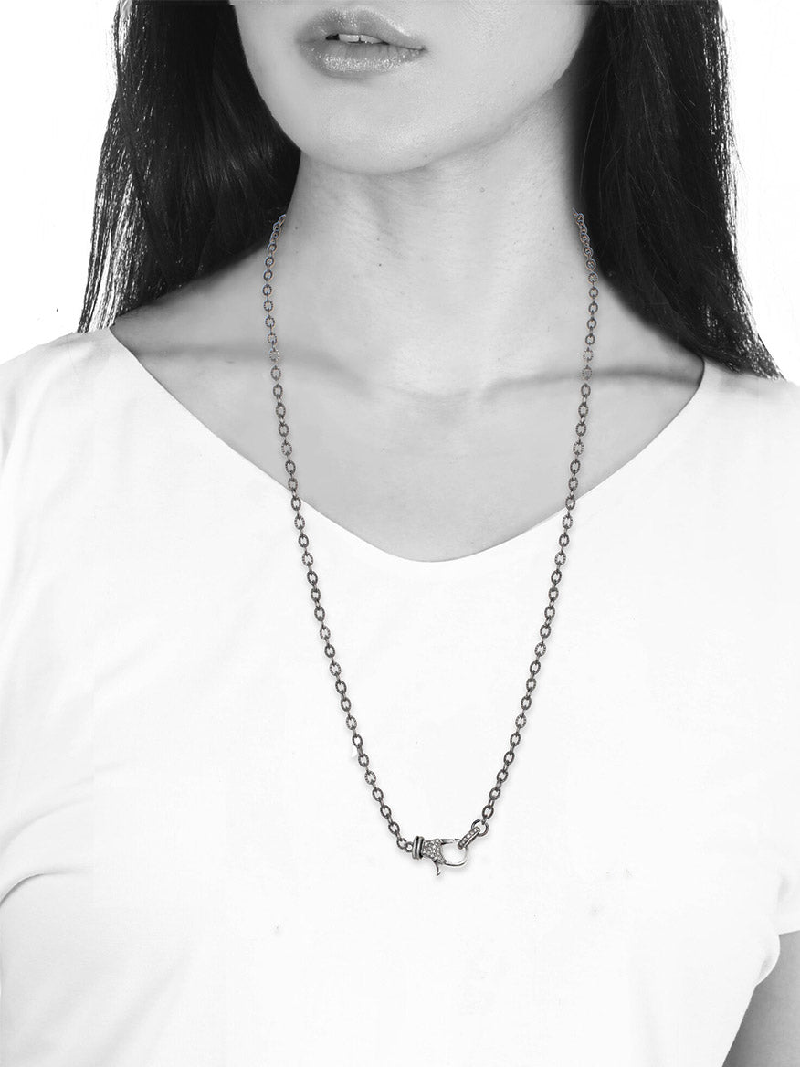 A monochrome close-up image of a woman wearing a white t-shirt and a Margo Morrison Rhodium Chain with Diamond Clasp - 24" necklace with a pendant.