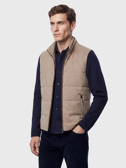 A man wearing the Maurizio Baldassari Arena Cashmere Vest in Brown Sugar over a navy button-up shirt and dark trousers stands against a plain light gray background—a refined look that seamlessly blends urban living with classic style.