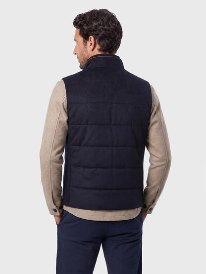 Man shown from behind wearing a beige long-sleeve shirt, navy pants, and the Maurizio Baldassari Arena Cashmere Vest in Dark Navy against a plain light background—an ideal look for urban living.