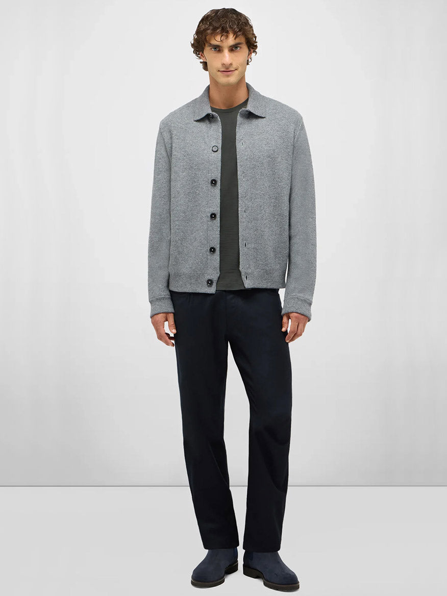 A man stands against a plain background wearing the Maurizio Baldassari Pique Knit Cashmere Blend Blouson in Light Grey, made in Italy, over a dark t-shirt, paired with dark trousers and shoes.