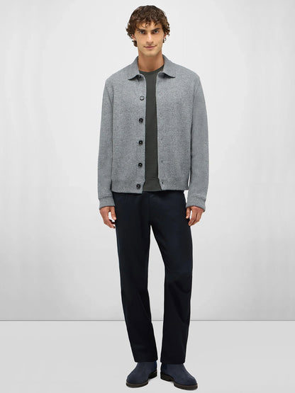 A man stands against a plain background wearing the Maurizio Baldassari Pique Knit Cashmere Blend Blouson in Light Grey, made in Italy, over a dark t-shirt, paired with dark trousers and shoes.