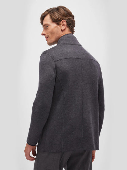 A man stands facing away against a plain light background, wearing the Maurizio Baldassari Jamaica Reversible Wool Swacket in Nightshadow Blue—a blazer-style jacket with a notch collar and visible seam details, crafted from extrafine merino wool for timeless appeal.