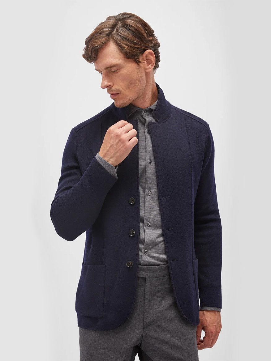 A man with brown hair wears the Maurizio Baldassari Jamaica Reversible Wool Swacket in Nightshadow Blue, crafted from soft merino wool, over a grey button-down shirt and grey trousers, set against a plain light background.