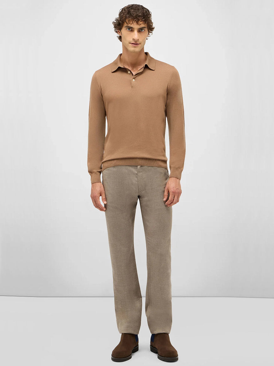 A man faces forward, wearing the Maurizio Baldassari 3-Button Long Sleeve Extrafine Wool Polo in Camel, light brown pants, and brown shoes against a plain light gray background.