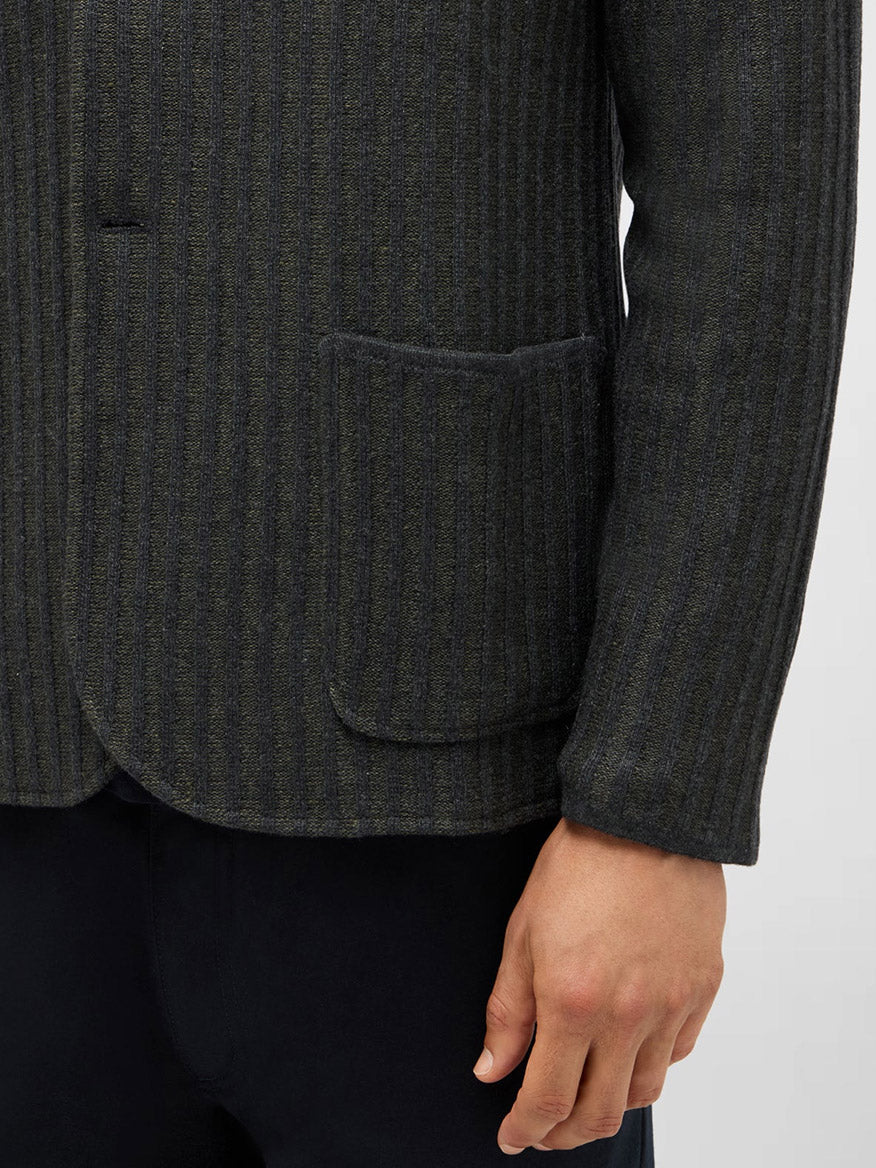 A close-up of a person's right arm in a Maurizio Baldassari Ribbed Knit Marled Shacket in Dark Green, featuring patch pockets, against a light background.