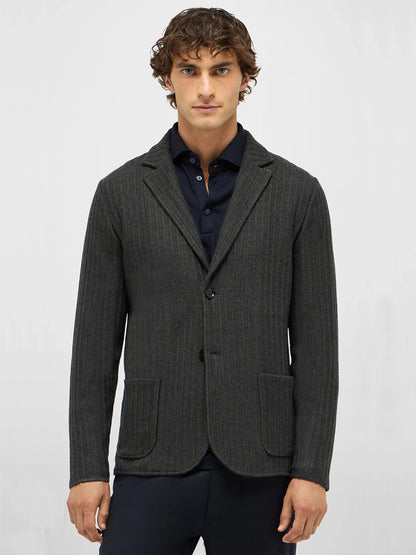A man with curly brown hair wears a Maurizio Baldassari Ribbed Knit Marled Shacket in Dark Green over a navy blue shirt, standing against a plain light background.
