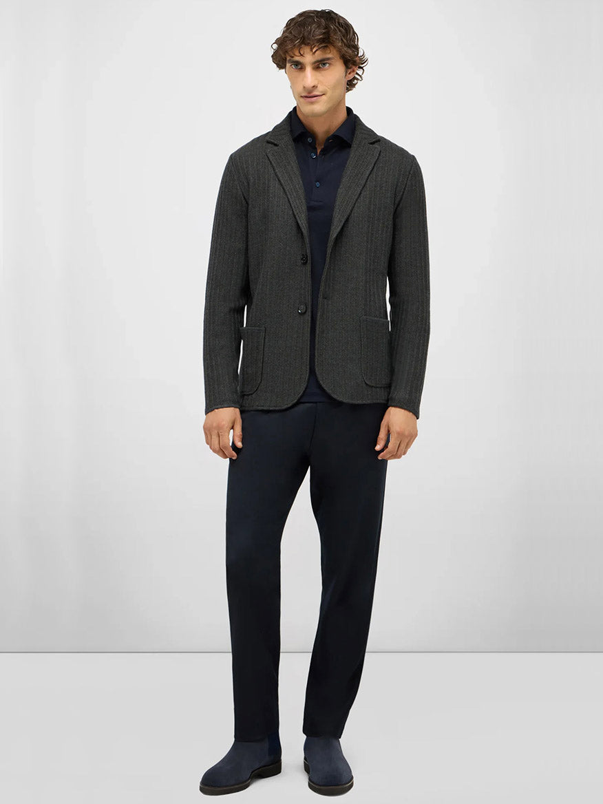 A man stands against a plain background wearing a Maurizio Baldassari Ribbed Knit Marled Shacket in Dark Green over a navy collared shirt, dark trousers, and grey shoes.