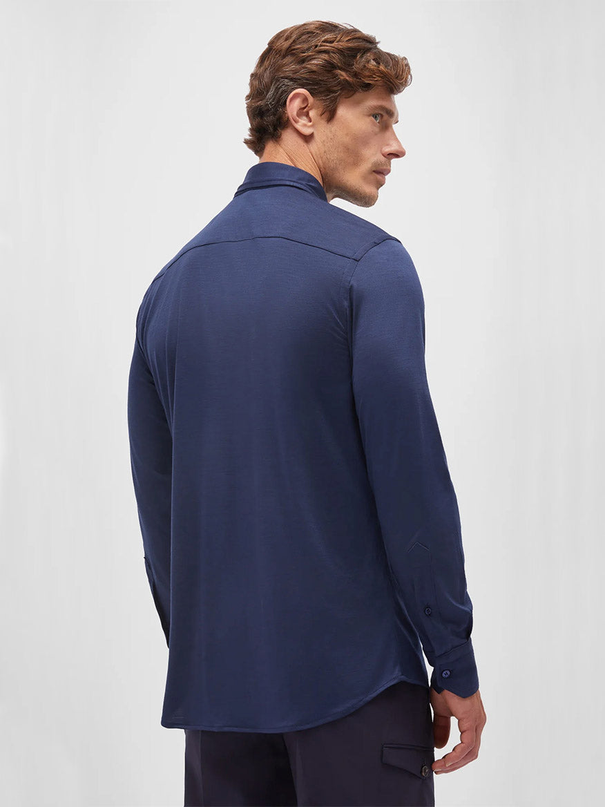 A man stands facing away, wearing the Maurizio Baldassari Santini Techmerino Wool Shirt in Blue with dark pants, set against a plain light background.