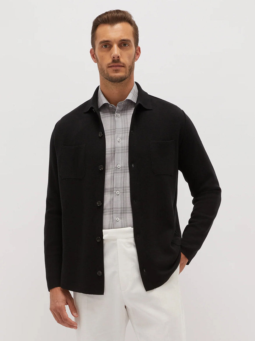 A man wearing a Maurizio Baldassari Silk & Cotton Overshirt in Black over a gray checked shirt and white pants, standing against a neutral background.