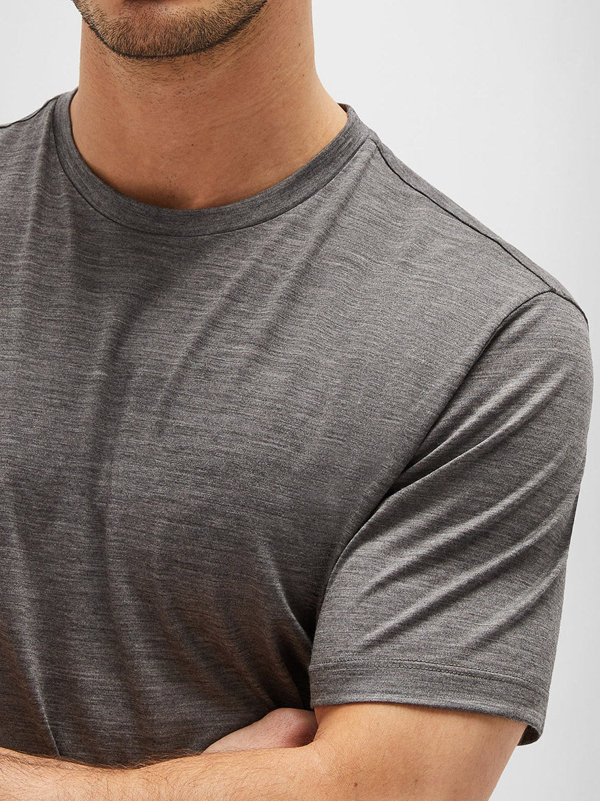 A person in a Maurizio Baldassari Linate Techmerino Short Sleeve T-Shirt in Medium Heather Grey is standing with arms crossed, showing a partial view of their torso and face.