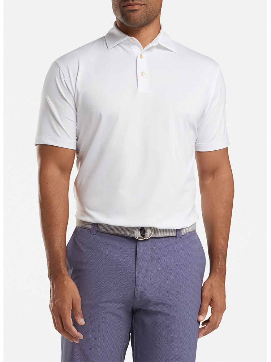 Man wearing a white Peter Millar Solid Performance Jersey Polo with UPF 50+ sun protection and grey pants with a belt.