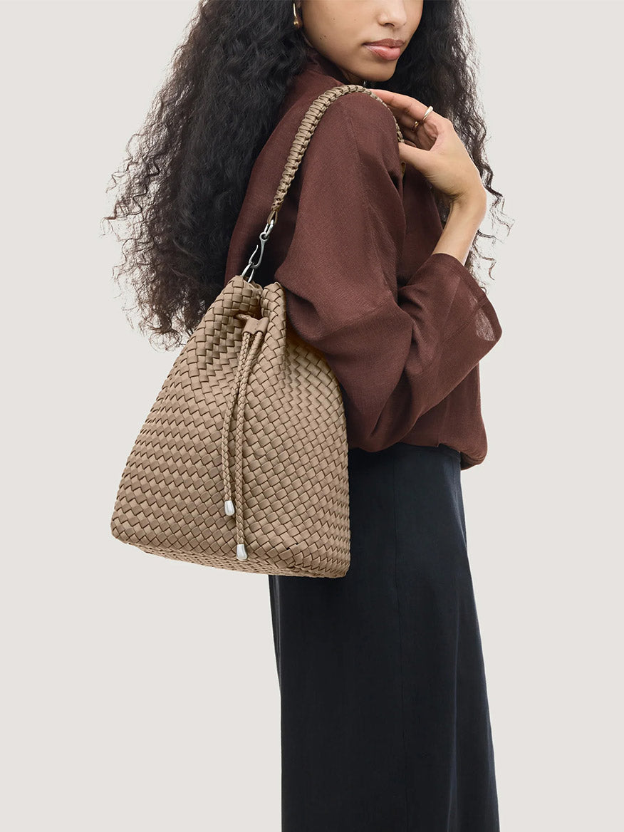 A person wears a handwoven beige Naghedi Mercer Large Bucket in Cashmere with a drawstring closure over their shoulder.