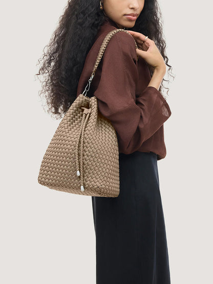 A person wears a handwoven beige Naghedi Mercer Large Bucket in Cashmere with a drawstring closure over their shoulder.
