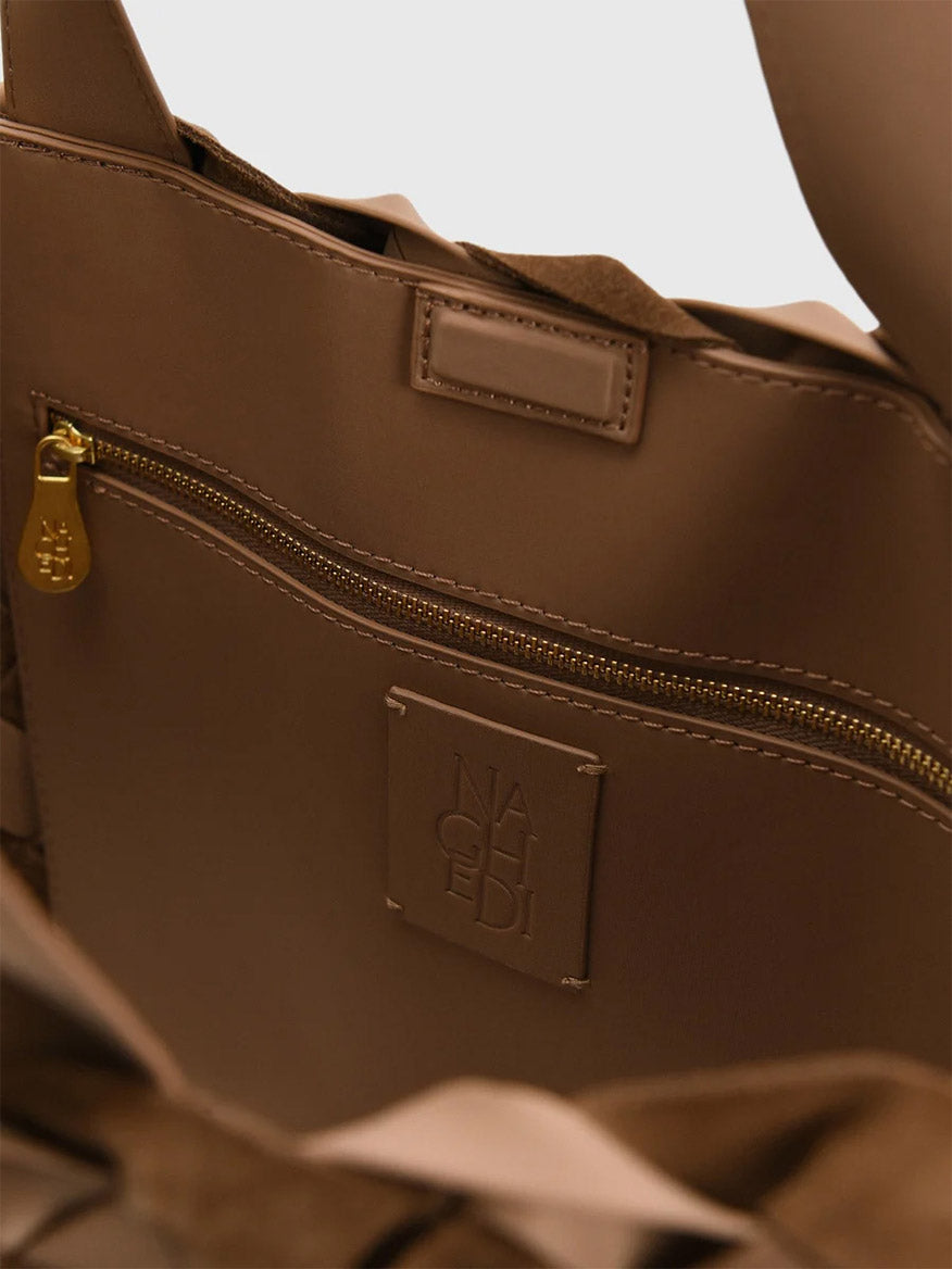 Interior of a brown Naghedi Como Shopper Tote Suede & Neoprene in Canyon, featuring a zippered pocket and a square logo patch embossed with the brand name.