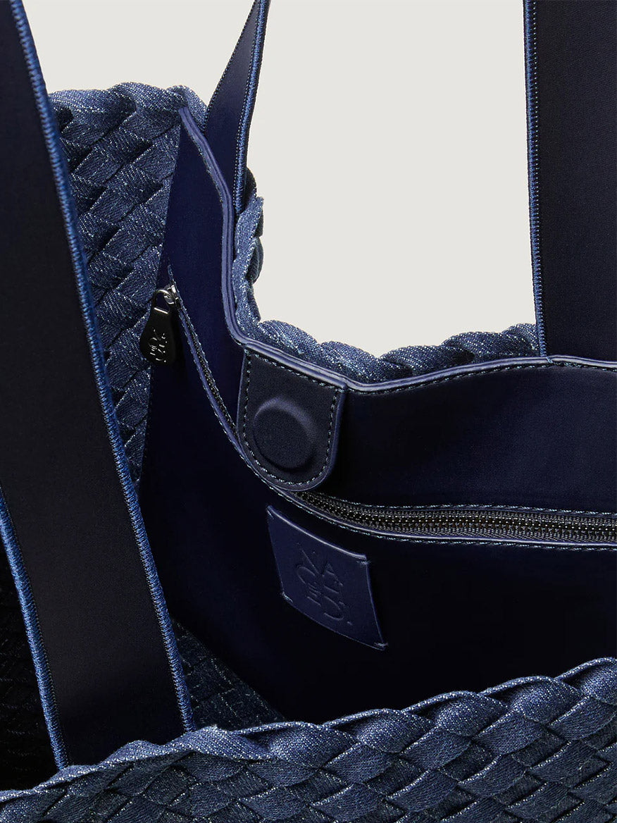 Close-up of the Naghedi Como Shopper Tote in Denim. This unisex, blue handwoven bag features a textured exterior, fabric straps, snap button closure, and a zippered inner pocket.