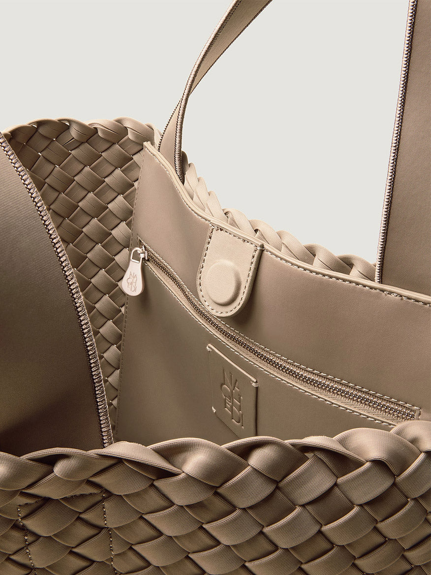 Close-up of the beige Naghedi Como Shopper Tote interior, featuring a zippered pocket with a branded pull tab and an embossed logo patch.