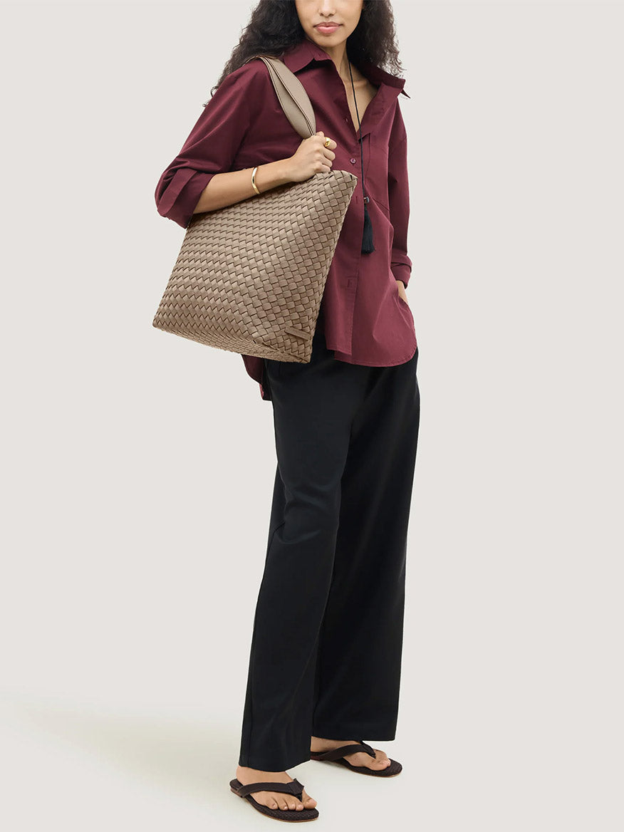A person carries a large, beige woven Naghedi Como Shopper Tote in Cashmere over their shoulder.