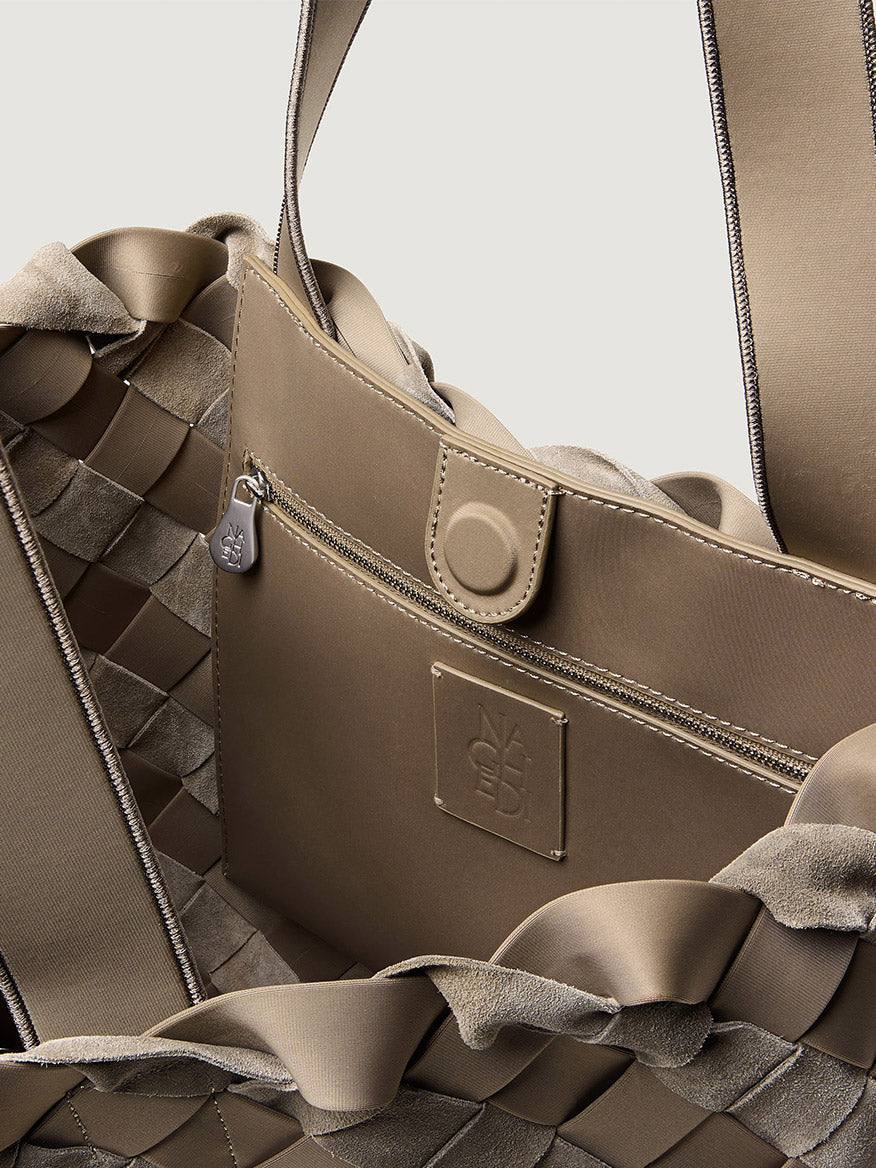 Close-up of a taupe Naghedi Como Shopper Tote Suede & Neoprene in Bluff, showing an internal zippered pocket with a magnetic closure and an embossed logo patch on this woven neoprene tote.