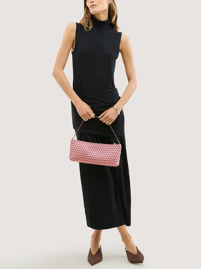 A person wearing a black sleeveless dress holds a Naghedi Gala Clutch Satin in Flor, a woven ballet pink clutch with a thin gold chain strap.