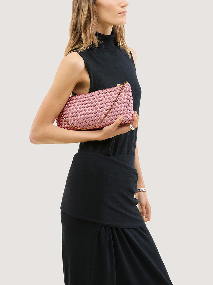A person holding a Naghedi Gala Clutch Satin in Flor, a ballet pink satin clutch with a thin gold chain strap.