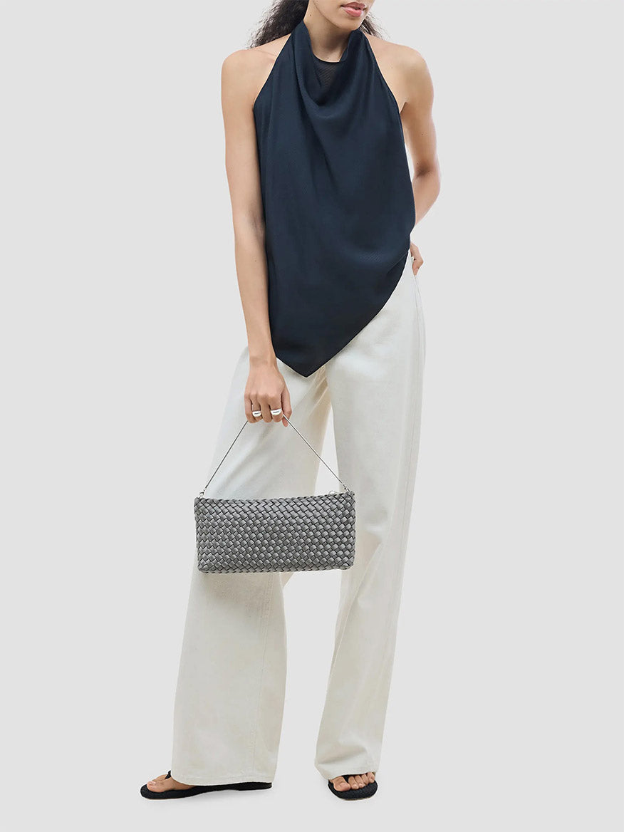 A person holding a grey woven rectangular Naghedi Gala Clutch Satin in Graphite by its thin metal handle.