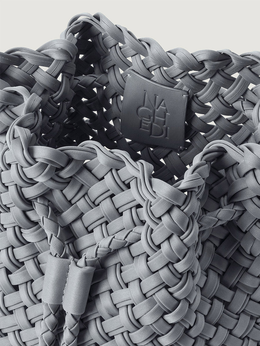 Close-up of a grey Naghedi Gramercy Bucket Double Weave in Marina, featuring a double-woven texture and a branded interior patch.