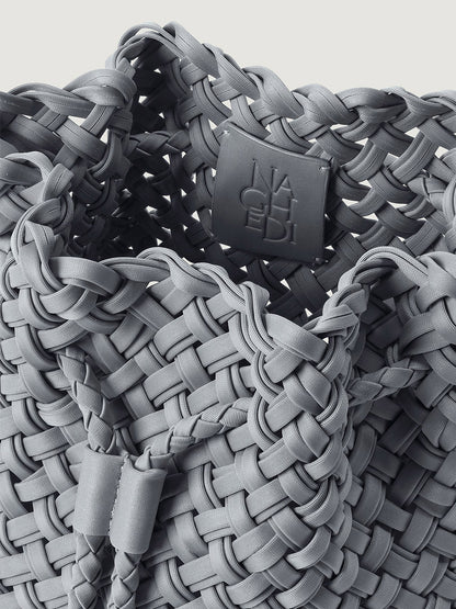 Close-up of a grey Naghedi Gramercy Bucket Double Weave in Marina, featuring a double-woven texture and a branded interior patch.