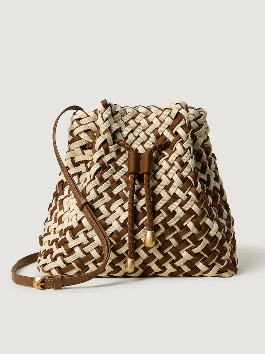 The Naghedi Gramercy Bucket Double Weave in Carmel is a chic brown and beige woven bag with a drawstring closure and slim shoulder strap, shown against a plain light background.