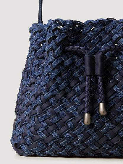 Close-up of the Naghedi Gramercy Bucket Double Weave in Indigo, a navy handwoven bag with a braided drawstring featuring metallic tips, styled in a classic bucket silhouette.
