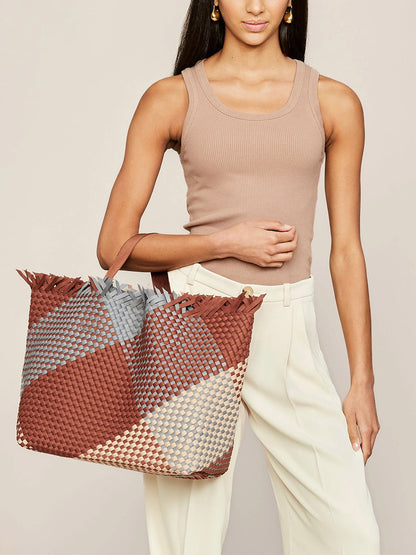 A woman holding a large, handwoven Naghedi Havana Beach Tote in Graphic Geo Taos Fringe with a geometric pattern.