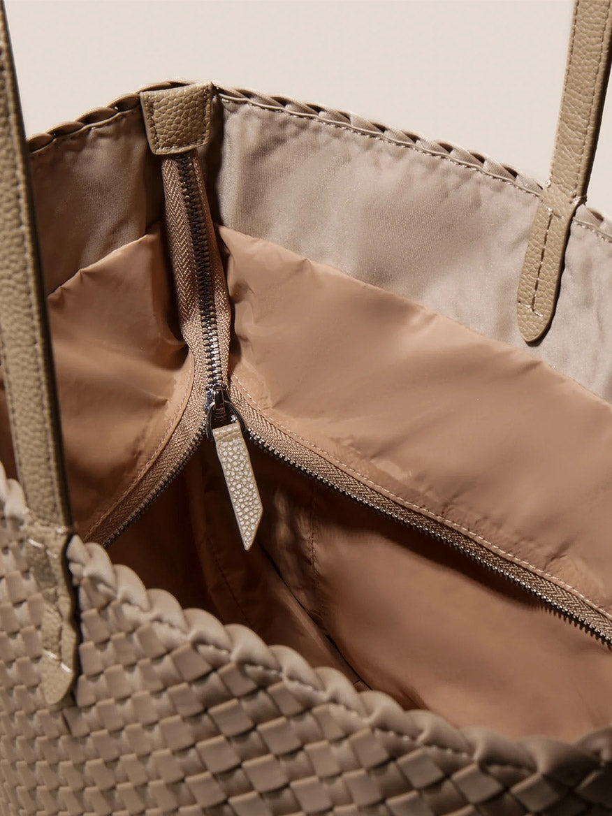 Close-up of the Naghedi Jetsetter Small Tote in Solid Cashmere, showcasing its beige woven vegan leather design, brown handles, and an interior open brown zippered pocket.