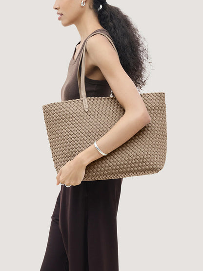 A person holds a large, beige handwoven neoprene Naghedi Jetsetter Small Tote in Cashmere under their arm.