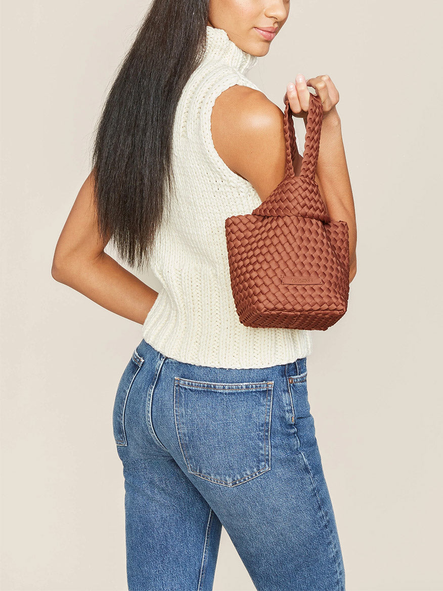 Woman in a white sleeveless top and blue jeans carrying a Naghedi Kyoto Clutch in Solid Adobe.