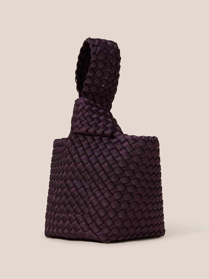 The Naghedi Kyoto Clutch in Solid Aubergine is a small, dark purple woven handbag made from handwoven neoprene, featuring a textured pattern and a short handle, ideal for enhancing evening ensembles against a simple backdrop.