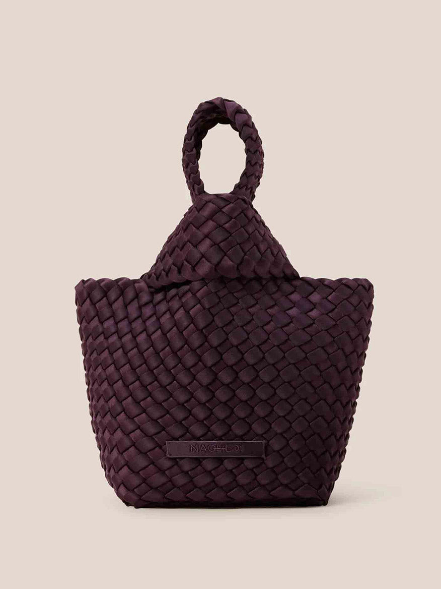 The Naghedi Kyoto Clutch in Solid Aubergine is exquisitely handwoven from neoprene, showcasing a textured surface and a looped handle against a plain beige background. It's the perfect accessory to complement evening outfits with its unique charm.