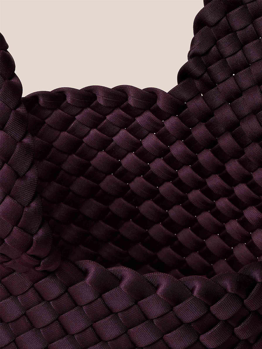 Close-up of the Naghedi Kyoto Clutch in Solid Aubergine, showcasing its handwoven basketweave pattern reminiscent of elegant evening attire, set against a neutral background.